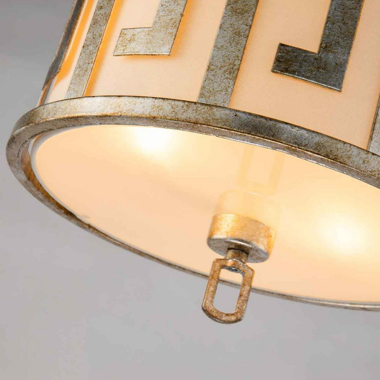 Close-up of the Lemuria 2 Light Duo-Mount Medium Pendant/Semi-Flush with an ivory fabric shade. The gold metal frame features a Grecian key motif and a weathered metallic finish. Adjustable height rods allow perfect positioning, while the illuminated fixture casts a warm glow.