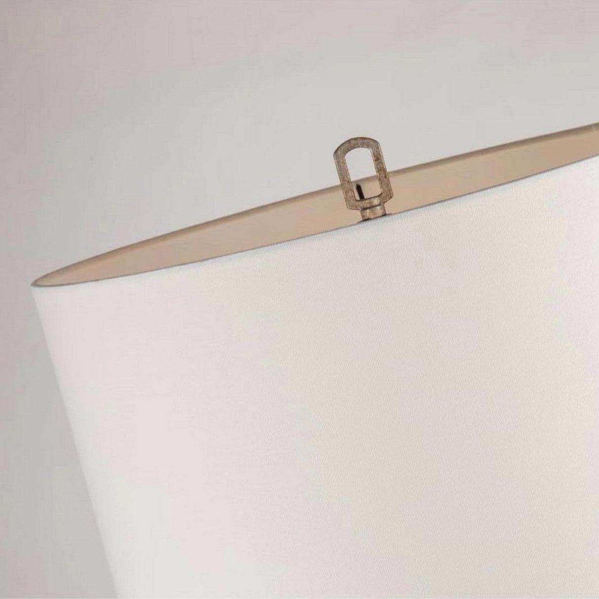 Close-up of an ivory lampshade with a gold-finish metal finial on top, highlighting the Lemuria 1 Light Table Lamp's elegance. The image emphasizes the texture and neutral color of the shade against a soft background.