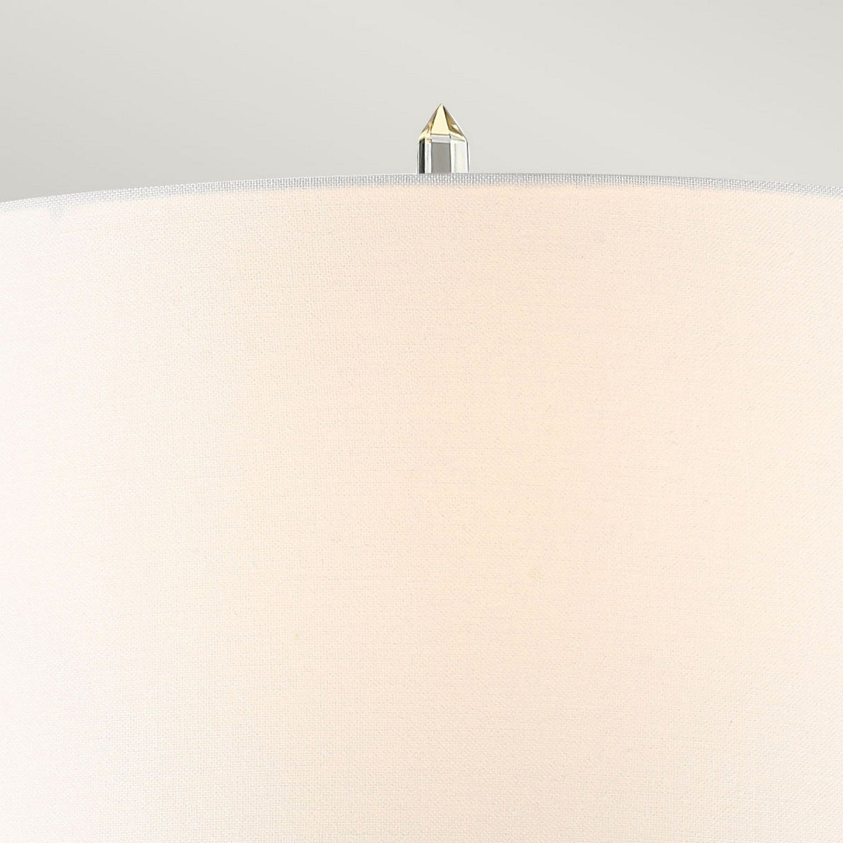 Close-up of the Sun King 1 Light Table Lamp featuring an ivory cylindrical shade topped with a small, pointed metal finial reminiscent of quartz points, set against a light gray background.