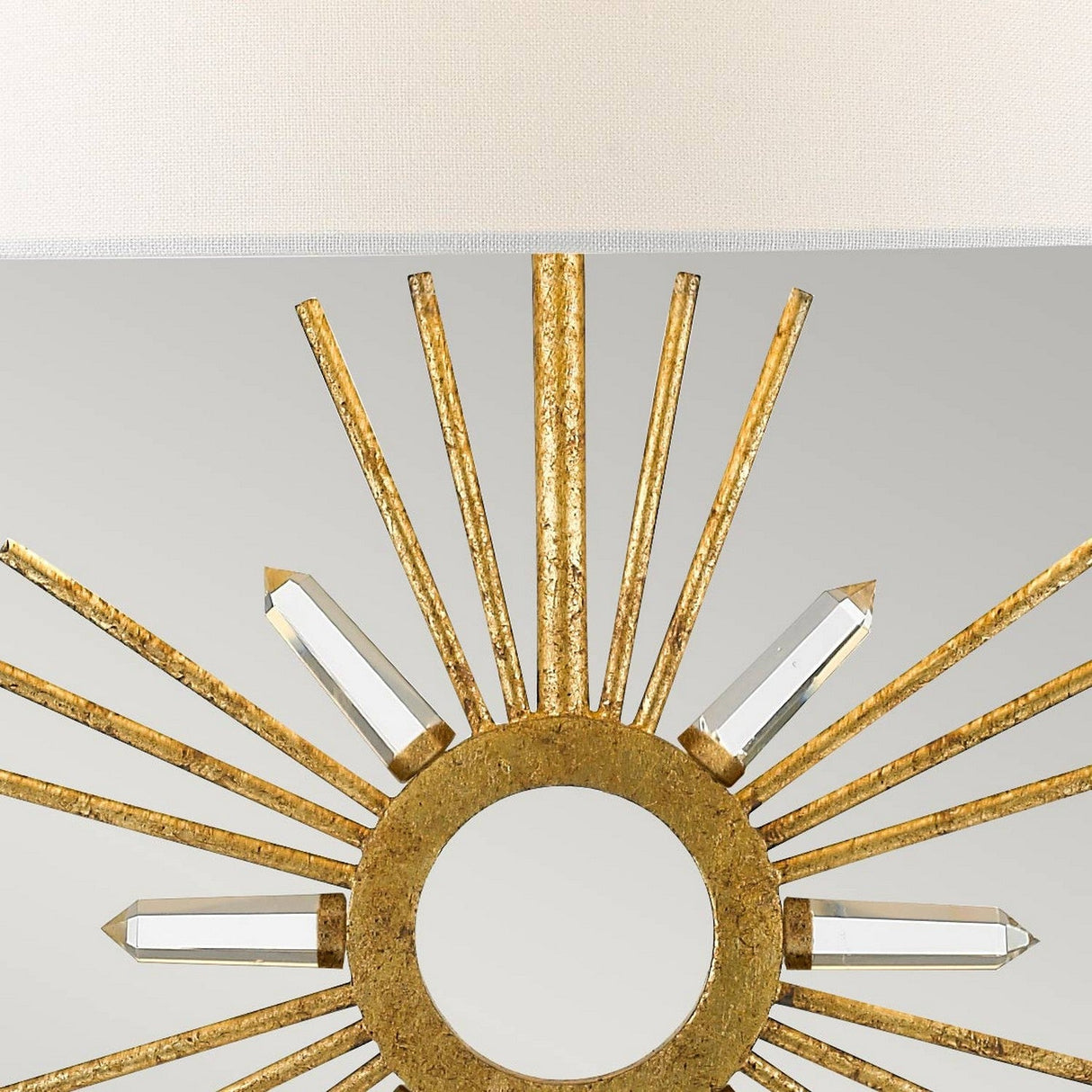 The Sun King 1 Light Table Lamp features a circular gold frame with radiating quartz points and clear crystal accents, creating a sunburst design set against a light grey background.