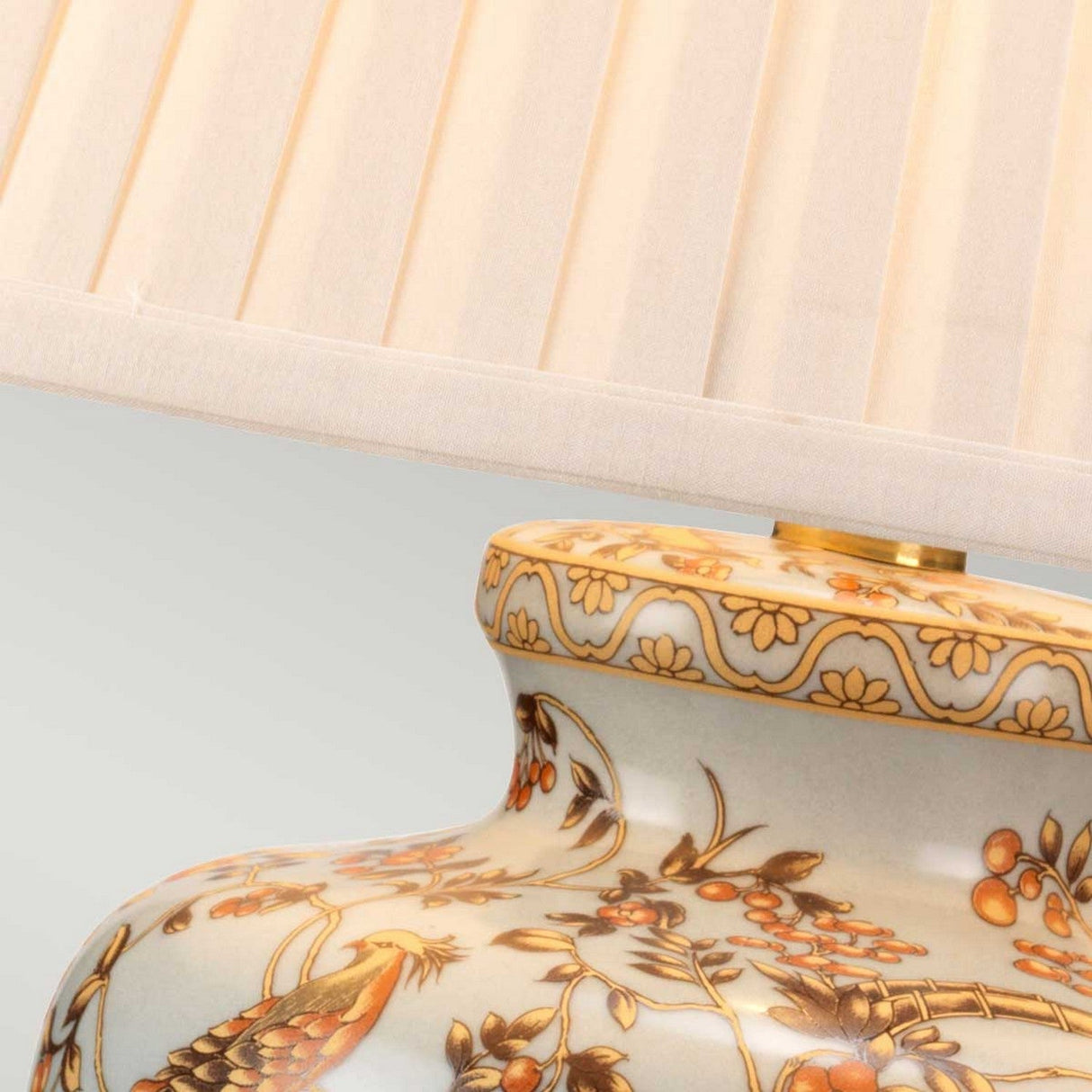 Close-up of an intricately designed base of the Gold Birds 1 Light Table Lamp in light blue and gold, showcasing delicate floral and bird patterns inspired by Chinese porcelain. The pleated cream-colored lampshade is partially visible at the top of the image.
