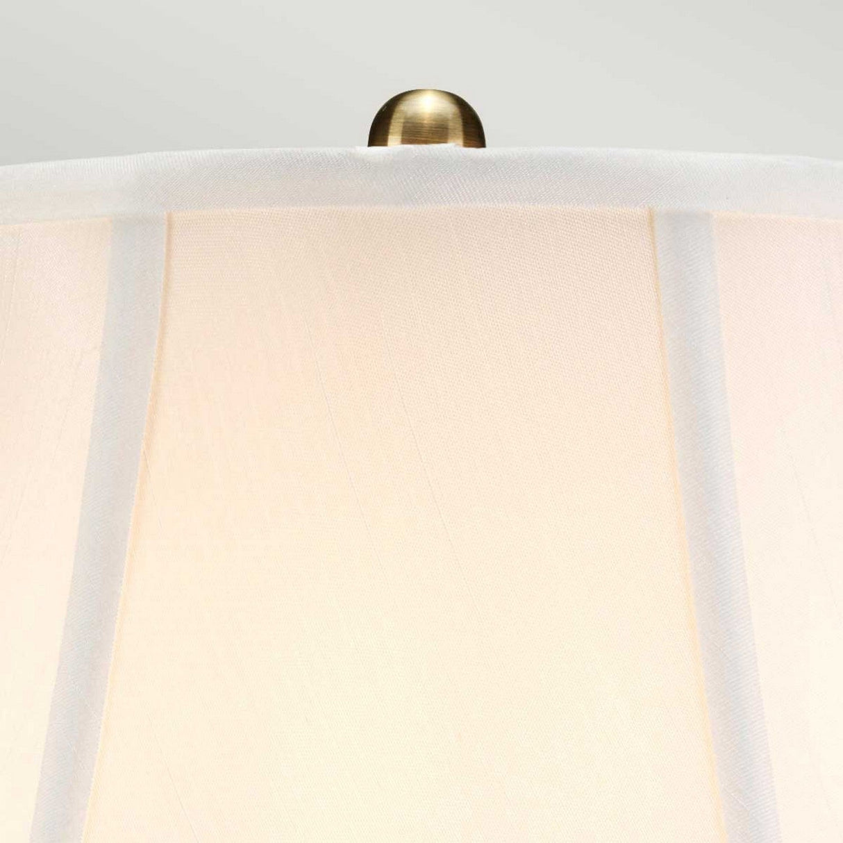 The Gold Thistle 1 Light Table Lamp - Gold features a close-up of a cream-colored lampshade with vertical seams and a brass finial on top, set against a neutral background. Beneath it, the Chinese porcelain base, elegantly adorned with a gold floral pattern, enhances its sophistication.