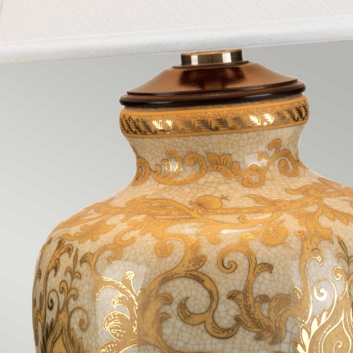 Close-up of the Gold Thistle 1 Light Table Lamp - Gold, showcasing its ornate ceramic base adorned with intricate golden floral patterns and a smooth, glossy finish. The lamp is completed with a partially visible fabric shade and features a dark brown neck with decorative detailing.