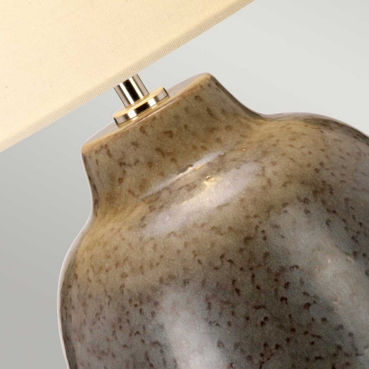 Close-up of the Grange Park 1 Light Table Lamp - Grey/Brown showcasing its ceramic base with a speckled, earthy reactive glaze. The base is adorned with a cream-colored fabric lampshade that offers soft ambient lighting.