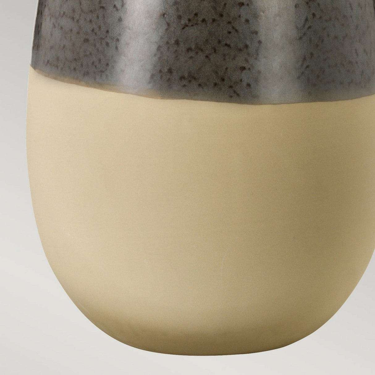 Close-up of the Grange Park 1 Light Table Lamp featuring a smooth, round shape. The upper section, ideal for ambient lighting effects, has a speckled gray tone, while the lower portion is a solid beige color. This lamp showcases a glossy finish on top and a matte finish on the bottom.