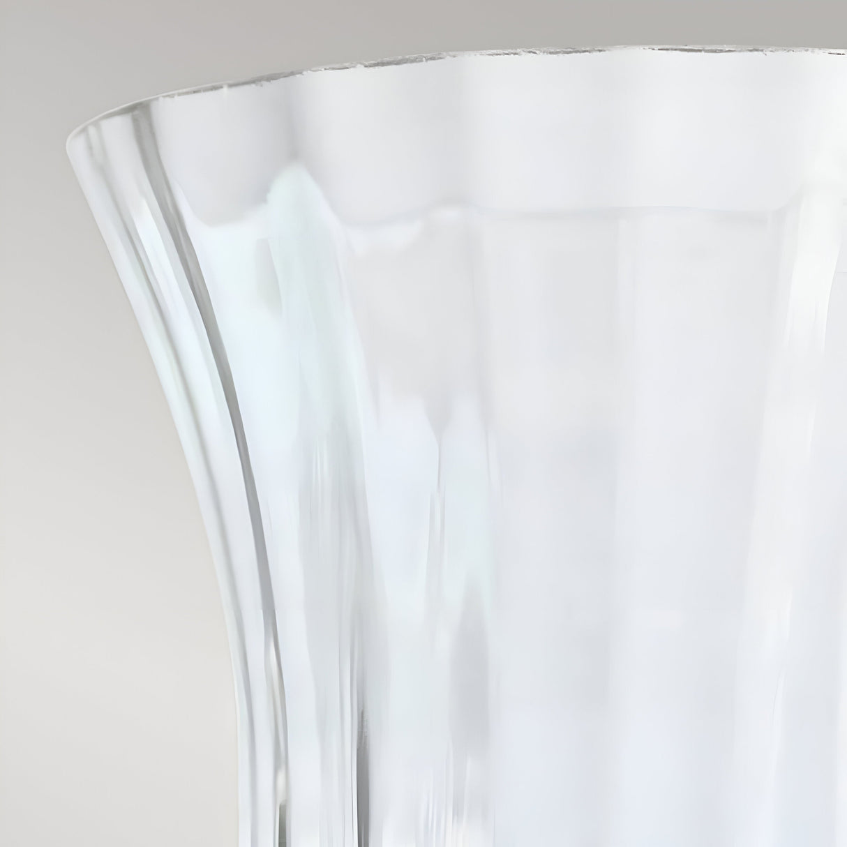 Close-up of a clear, glass vase with a flared top and vertical ridges, reminiscent of the Glass Shade Optional For Hinkley Cambridge - Clear Glass. The vase is empty and set against a plain light gray background, highlighting its elegant contours akin to refined lighting design.