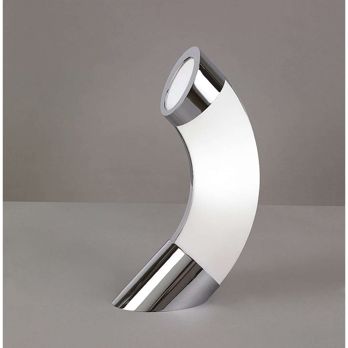 The Guss LED Table Lamp 15K 2700K features a tubular, arching shape and minimalist design in polished chrome with white acrylic, standing on a gray surface against a plain gray background. Energy efficient with a modern, curved look.