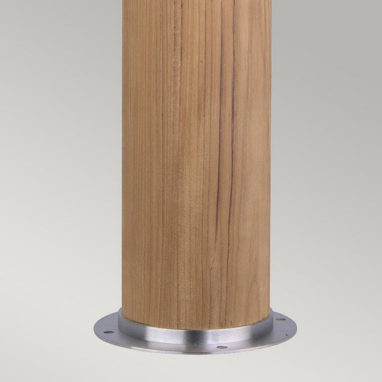 Close-up of the Poole 1 Light Bollard in light brown, crafted from Malaysian teak with a smooth finish. It features a metallic circular base made from marine grade 316 stainless steel, complete with several mounting holes. The background is a plain, light gray color.