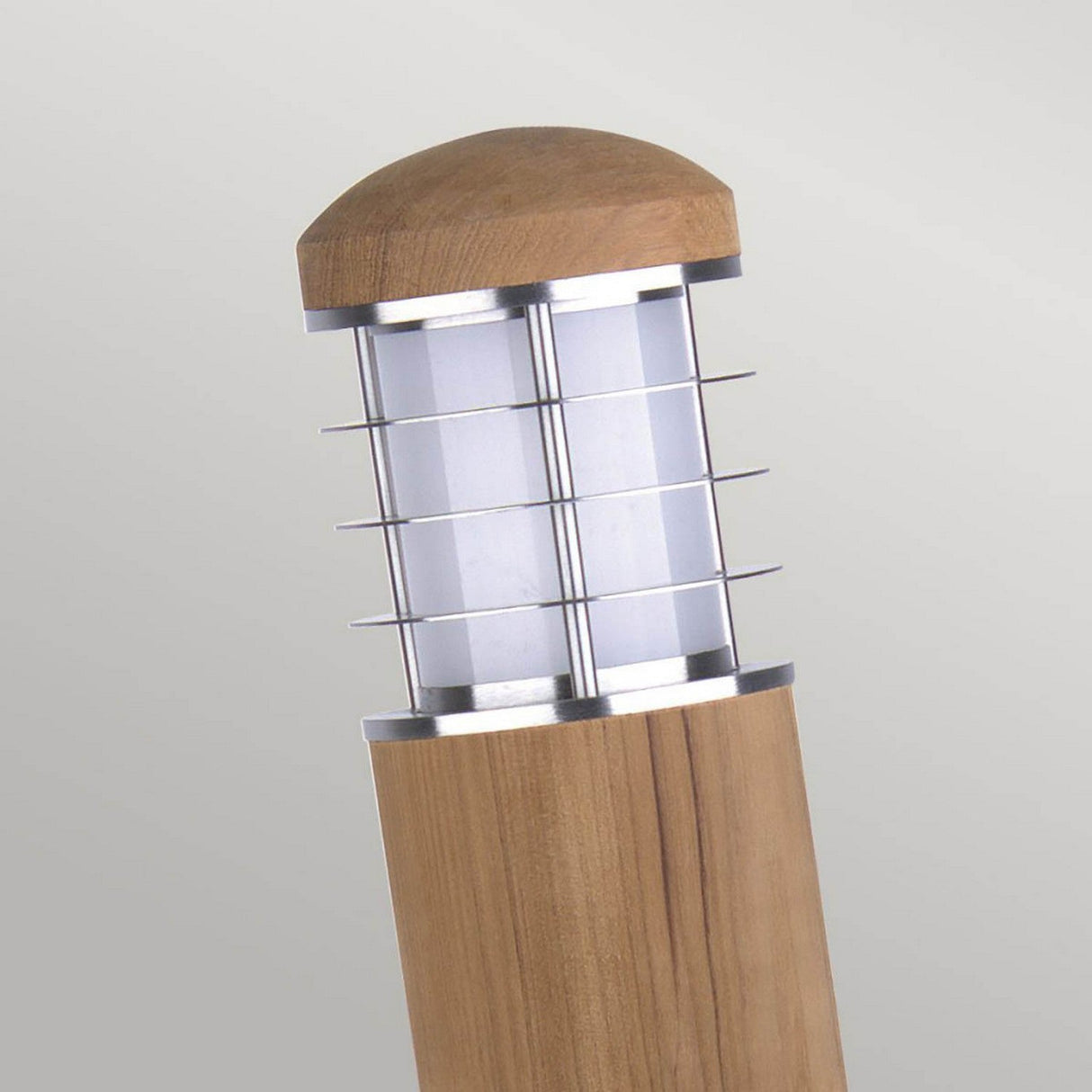 The Poole 1 Light Mini Bollard in light brown features a wooden design with a cylindrical shape, showcasing a transparent central section and metallic horizontal bars made from marine-grade 316 stainless steel for added protection. This outdoor lighting fixture is topped with a dome-shaped wooden cap and is displayed against a plain gray background.