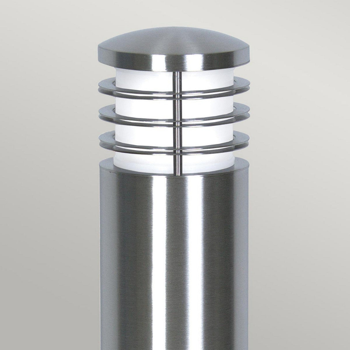 The Sandbanks 1 Light Bollard in silver is a contemporary outdoor lighting fixture featuring a cylindrical design with horizontal rings encircling a frosted light diffuser, and it has an IP44 rating. Its sleek stainless steel finish makes it perfect for placement against a neutral backdrop.