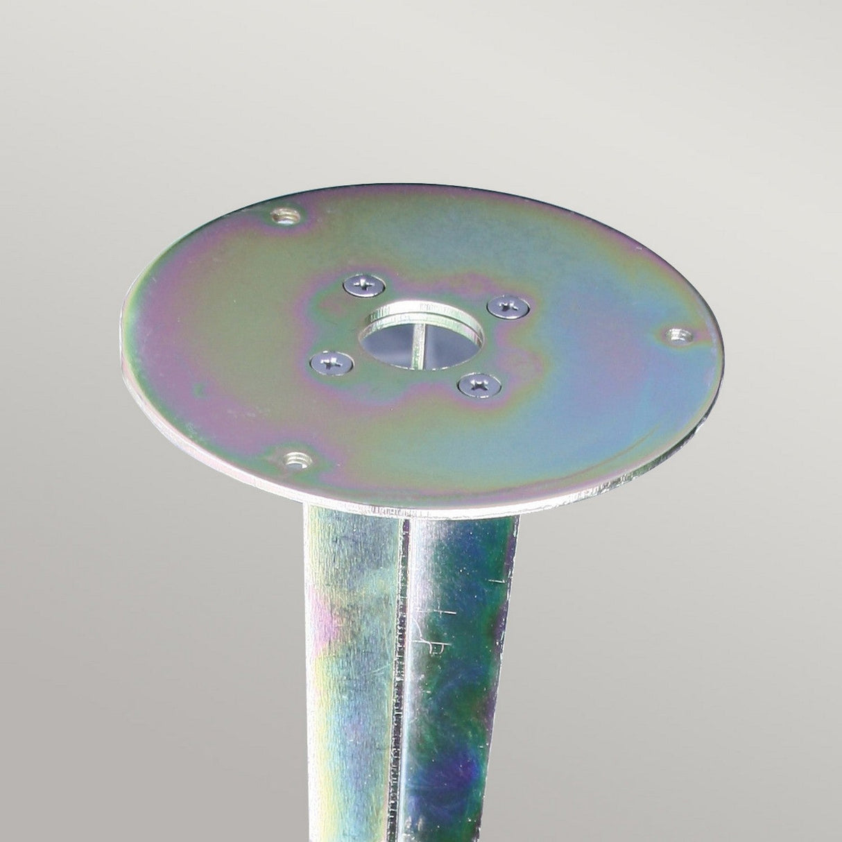 A metallic flange featuring a circular plate with multiple holes, connected to a vertical cylindrical rod, has an iridescent finish that reflects various colors against a neutral backdrop. Named the Spike for Sandbanks & Poole Bollards, it is ideal for enhancing Outdoor Lighting Solutions.