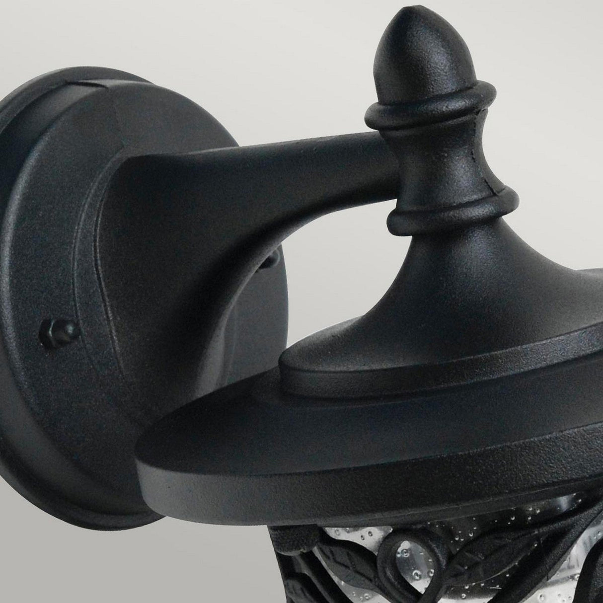 A close-up of the Burford 1 Light Outdoor Wall Lantern in black shows its elegant, wall-mounted design crafted from cast aluminum. Featuring a decorative cap and clear glass panels, this classic light fixture is enhanced with an IP44 rating for durability against the elements. The background is neutral and softly blurred.