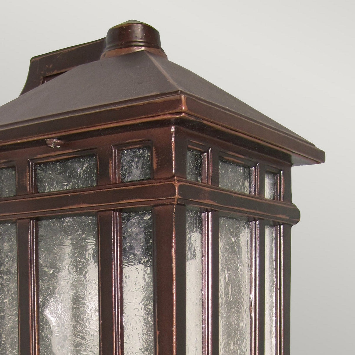 Close-up view of the Chedworth 1 Light Outdoor Wall Lantern - Bronze, featuring a vintage design with its cast aluminum construction, bronze finish, and textured glass panels. The lantern's pyramid-shaped top showcases its classic style against a plain background.
