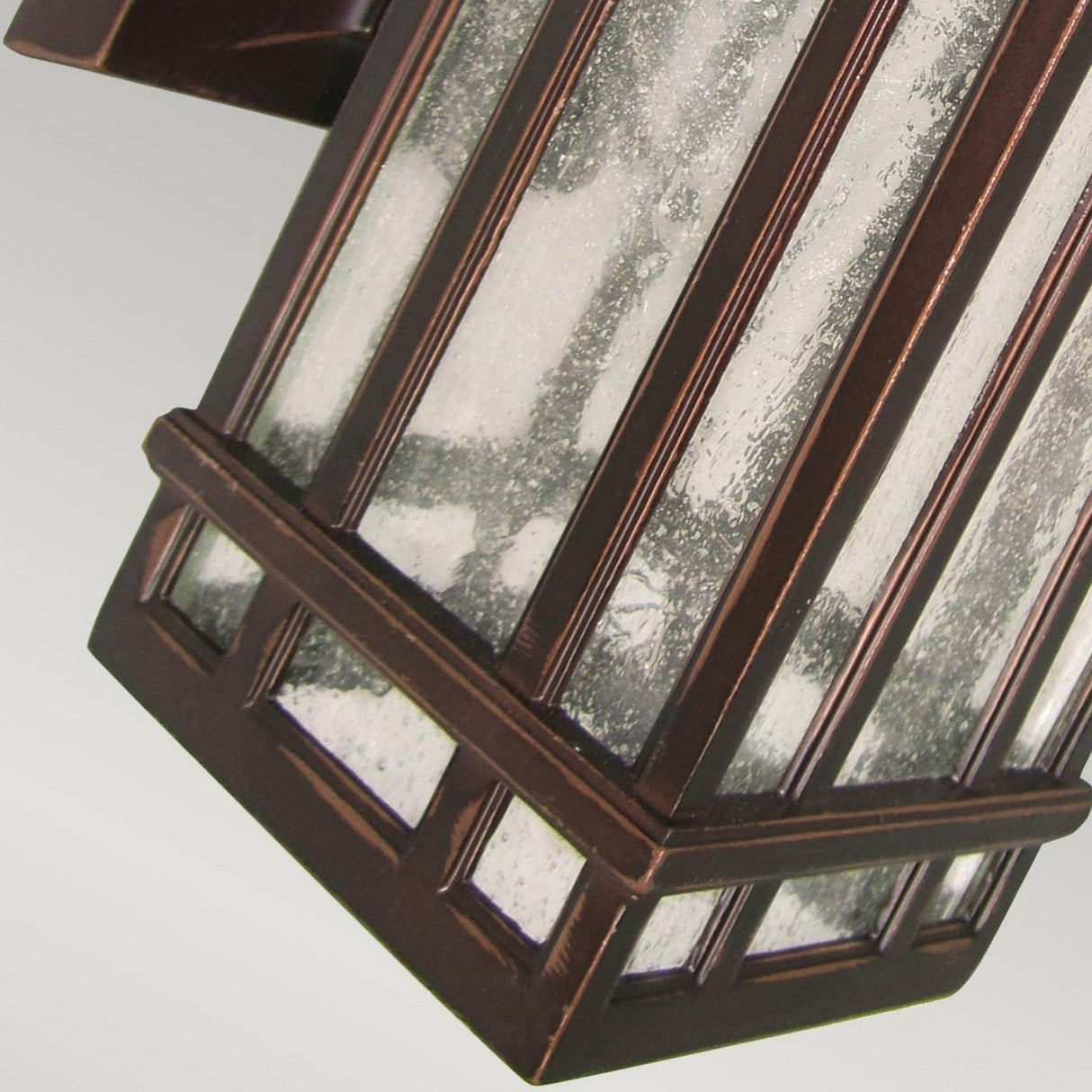 Close-up of the Chedworth 1 Light Outdoor Wall Lantern, highlighting its vintage style with a bronze finish and frosted glass panels. The lantern's durable cast aluminum frame showcases rectangular patterns, positioned diagonally against a light gray background.