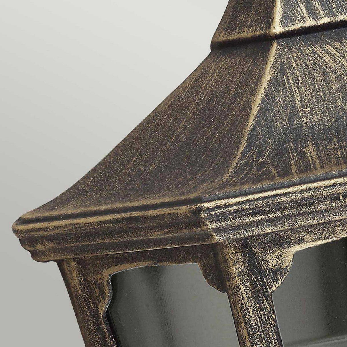 Close-up of the Cricklade 1 Light Outdoor Half Lantern in a black and gold finish, displaying its weathered, metallic appearance. Crafted from cast aluminium, it boasts a pointed roof and window-like panels that highlight its rustic and vintage design against a soft, neutral background. Perfect for IP44 rated lighting needs.