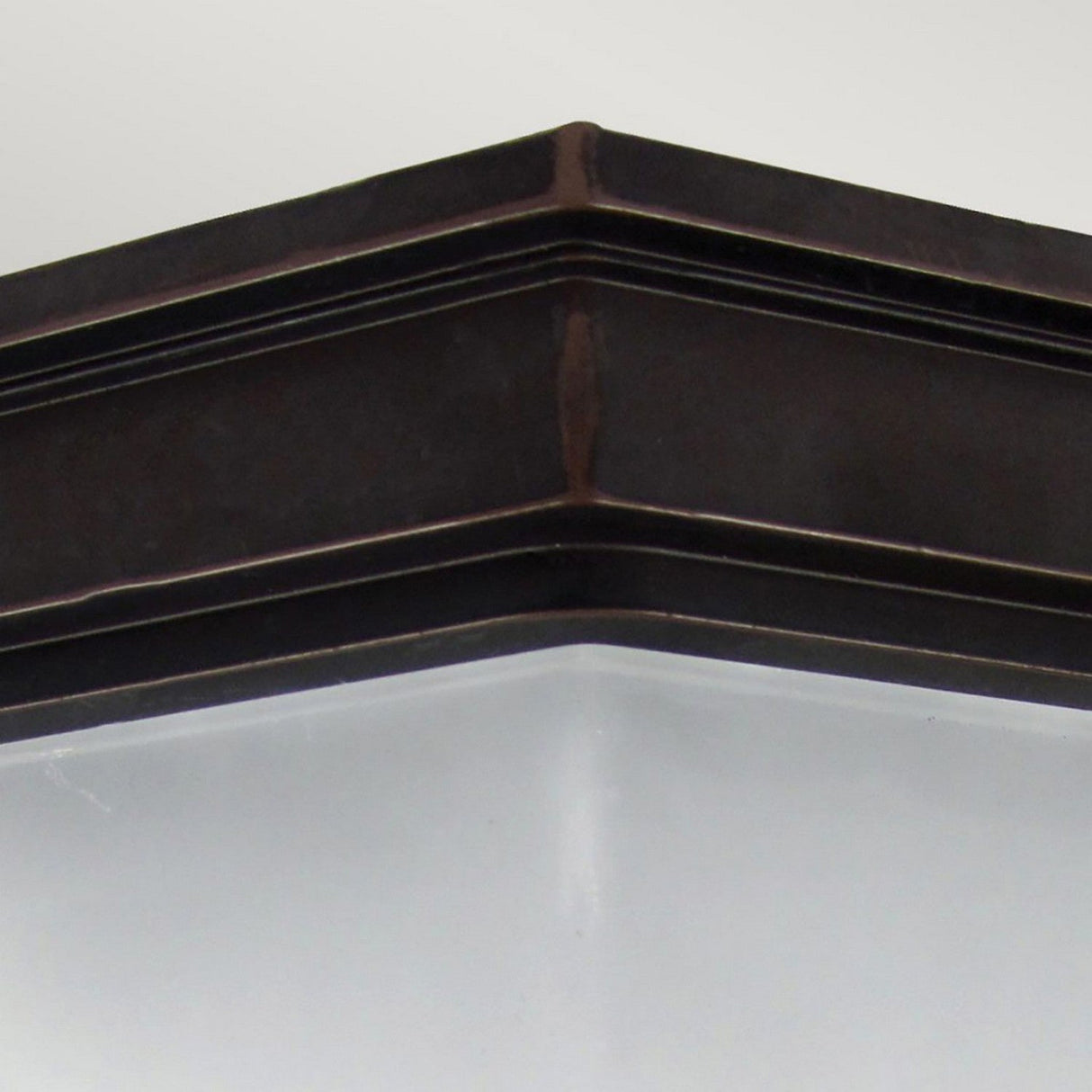 A detailed shot showcases the Fairford 1 Light Outdoor Flush Lantern in bronze, featuring a cast aluminum frame paired with frosted glass. The rectangular design provides gentle and diffused illumination, with the image capturing one corner of the fixture against a simple white ceiling, emphasizing its sophisticated style.