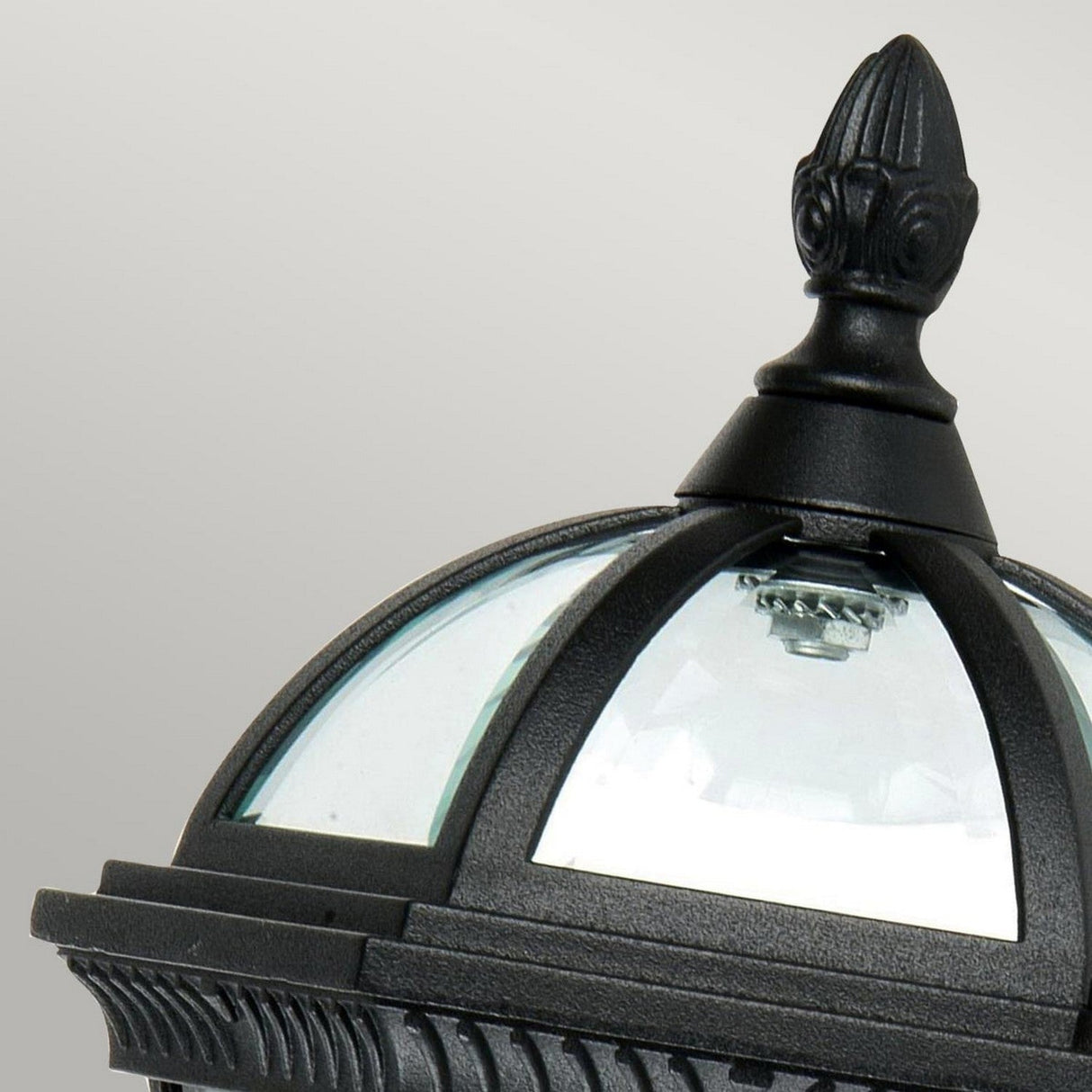 Close-up of the Ledbury 1 Light Wall Lantern - Black crafted from cast aluminum against a light gray background. The lantern showcases a rounded top with arched glass panels and intricate detailing, exemplifying exquisite decorative exterior lighting.