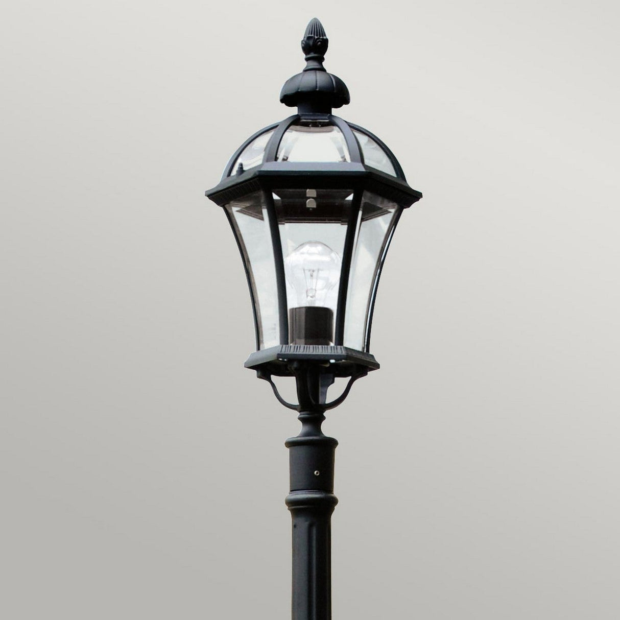 The Ledbury 1 Light Lamp Post - Black is a black vintage-style lantern crafted from cast aluminum, showcasing a clear glass casing and a visible light bulb. This decorative exterior lighting piece is elegantly displayed against a plain gray background.