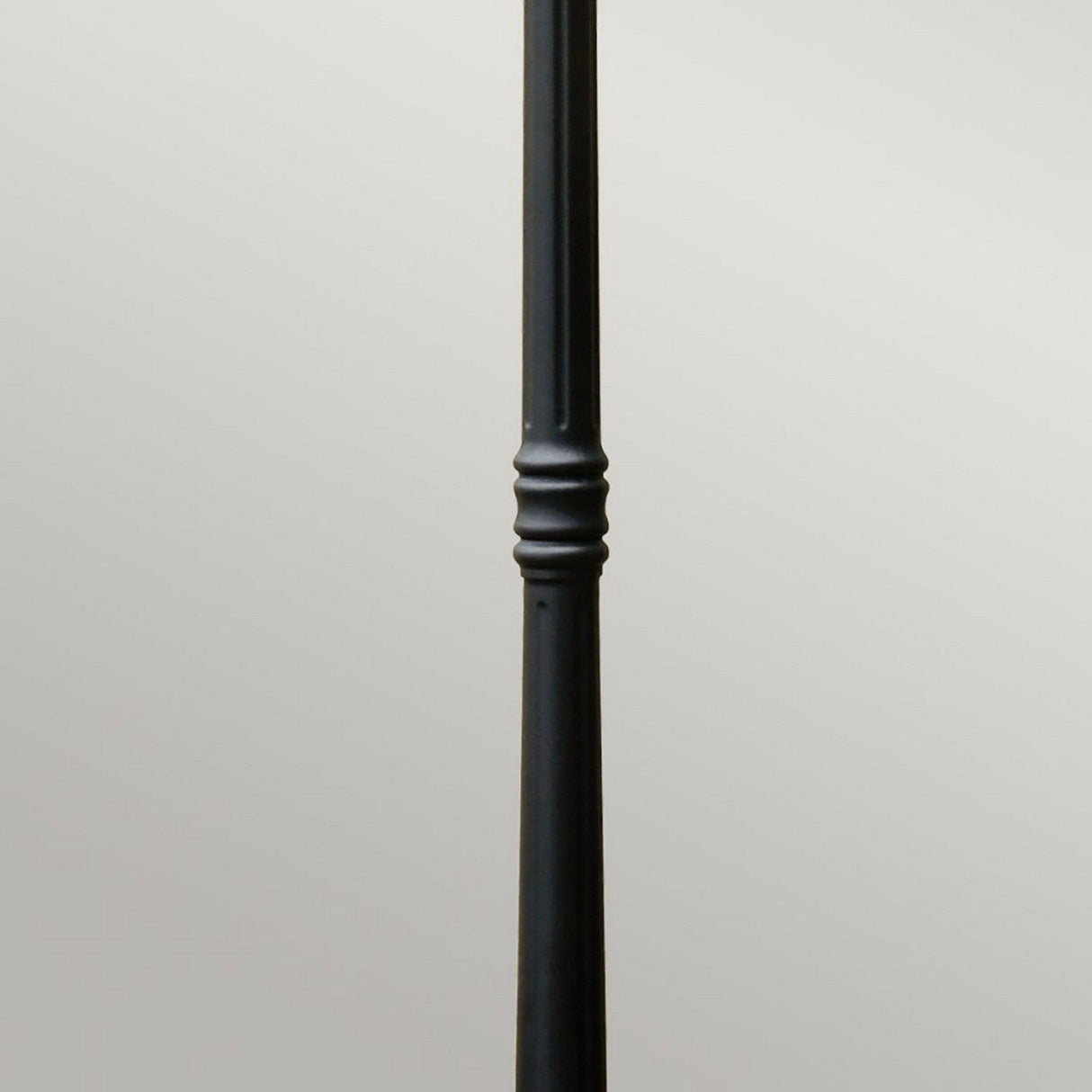 The Ledbury 1 Light Lamp Post in black features a single, tall metal pole with an elegant decorative design in the middle, evoking a heritage lantern style against a plain gray background.