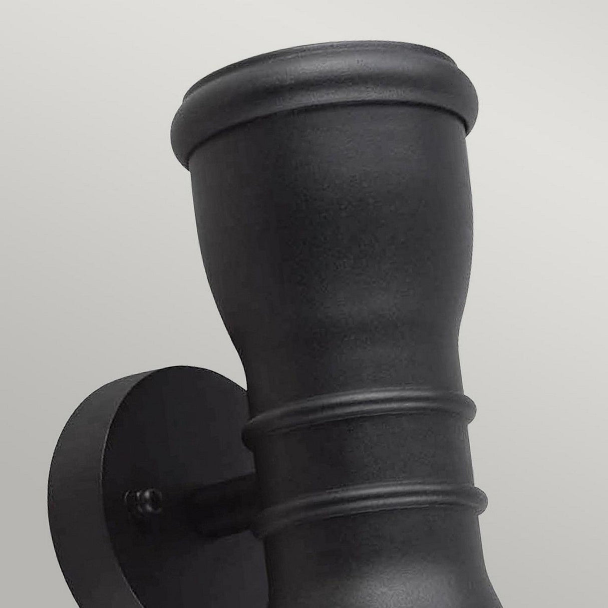 Close-up of the Malvern 2 Light Up & Down Lantern - Black, showcasing its cylindrical shape and matte finish in cast aluminum. The fixture features two ridged bands near the top and is mounted on a circular base against a light gray background, providing decorative exterior lighting reminiscent of a Heritage Lantern.