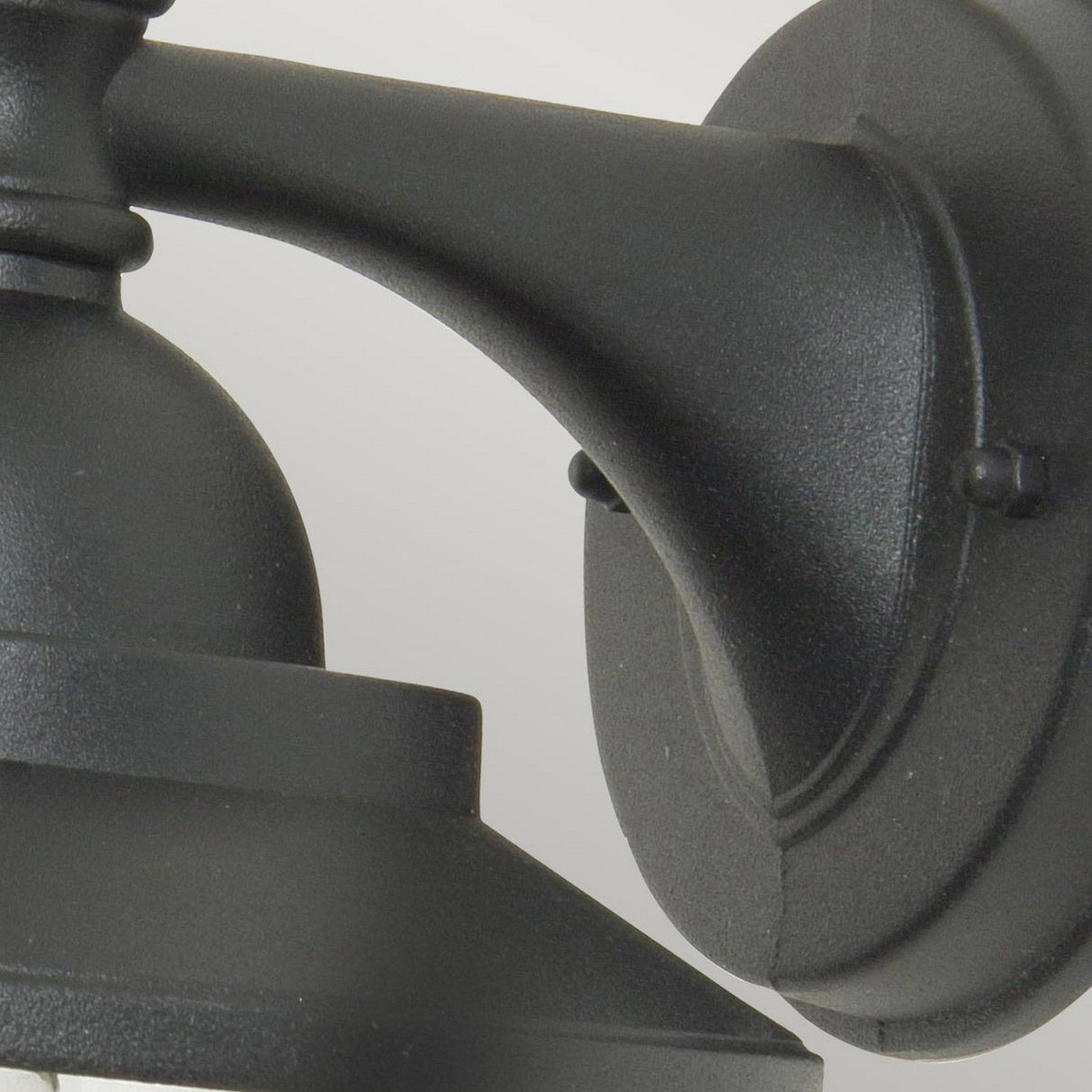 Close-up image of the Sandown 1 Light Outdoor Wall Lantern in black, featuring a matte finish and crafted from cast aluminum. The photo highlights the curved arm and part of the lantern’s top, showcasing its simple and classic design against a neutral background.