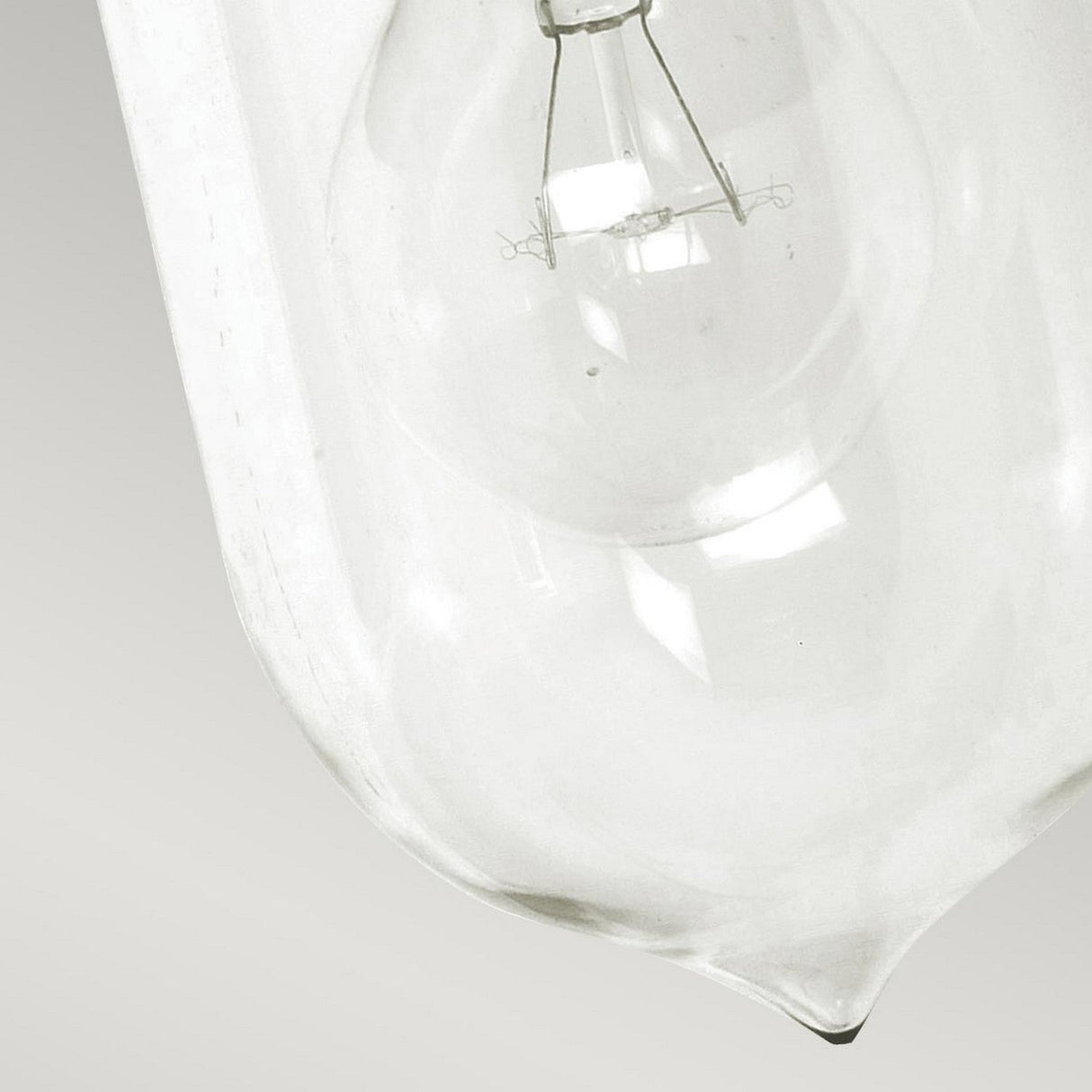 Close-up of a clear glass light bulb positioned at a diagonal angle against a plain white background, evoking the elegant design of the Sandown 1 Light Outdoor Wall Lantern - Black. The internal filament and structure of the bulb are clearly visible, capturing a classic aesthetic reminiscent of cast aluminum fixtures.