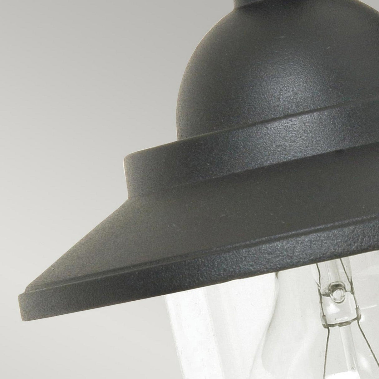 Close-up of the Sandown 1 Light Outdoor Wall Lantern in black, featuring a cast aluminum top and clear glass casing, set against a gray background.