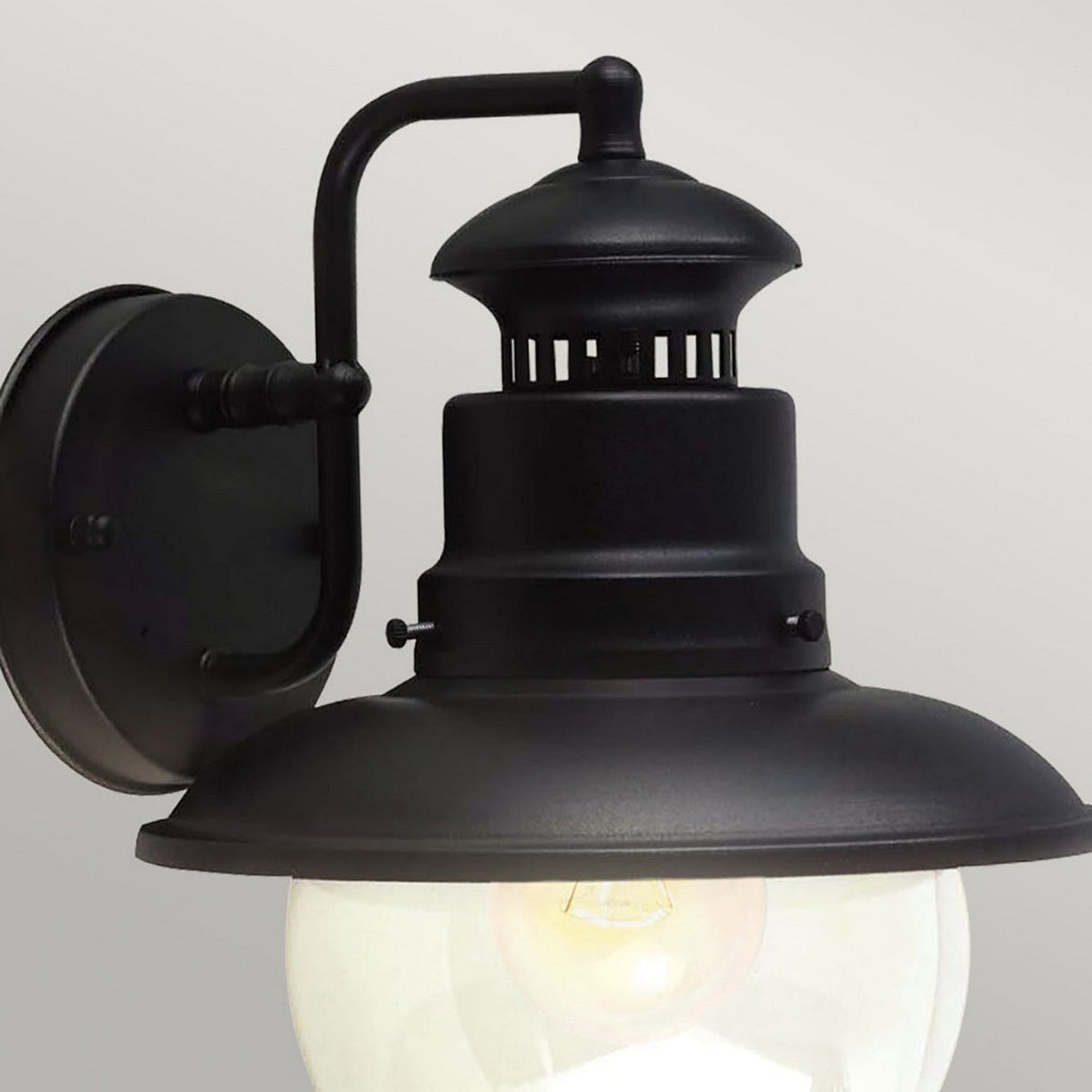 The Shipston 1 Light Outdoor Wall Lantern - Black boasts a classic vintage-style design with a dome-shaped cover and frosted glass bulb, all elegantly displayed against a simple gray backdrop.