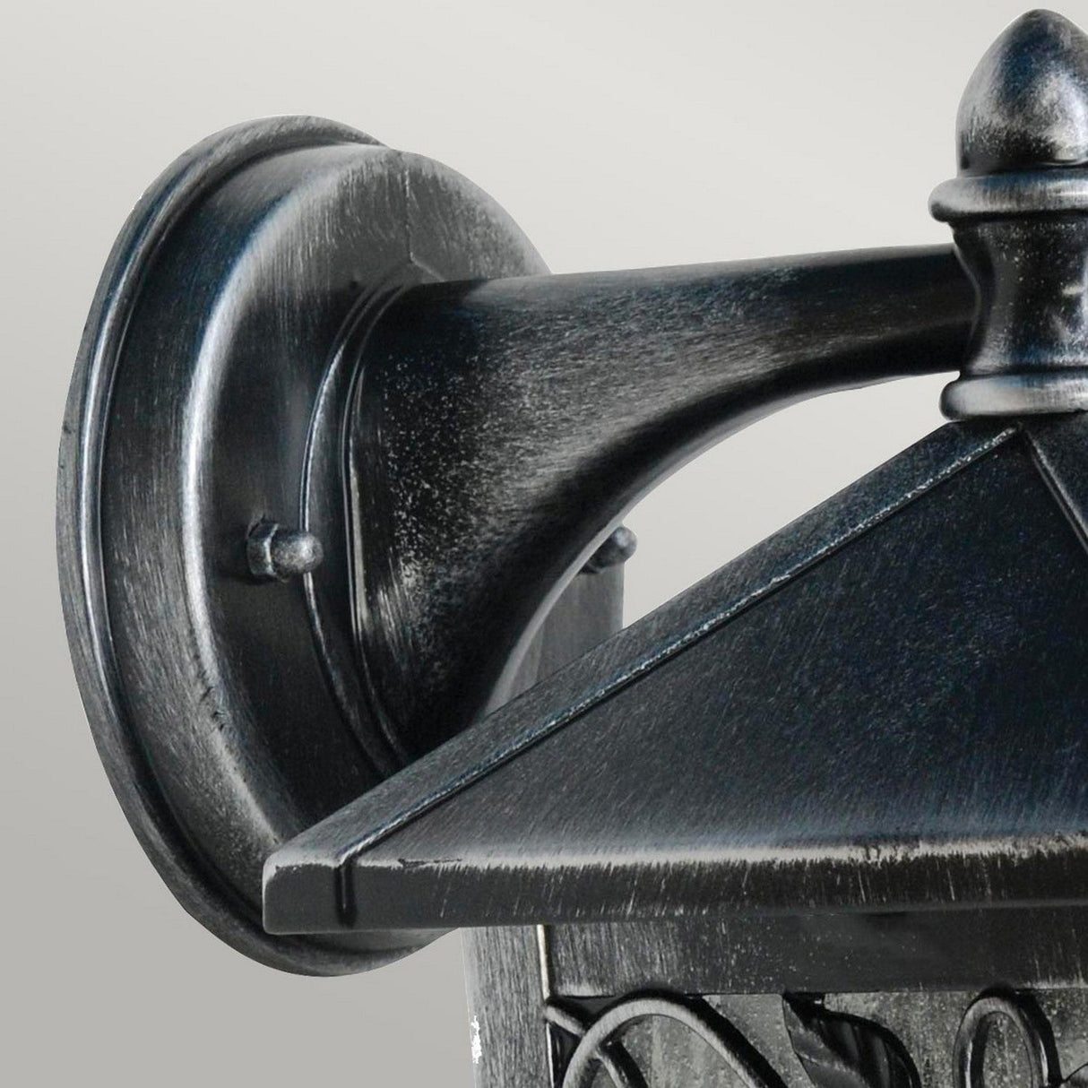 Close-up of the Winchcombe 1 Light Outdoor Wall Lantern in black, crafted from cast aluminum. This IP44 rated fixture features a decorative triangular top and mounted base, highlighted by a textured, weathered finish against a light gray background.