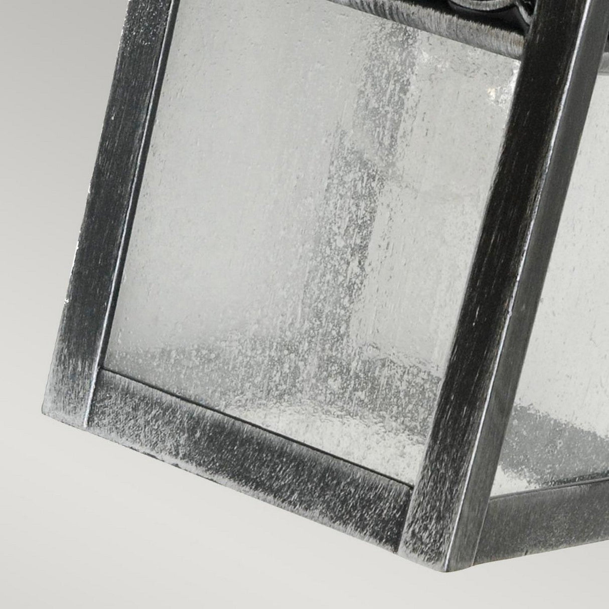 Close-up of the Winchcombe 1 Light Outdoor Wall Lantern in black, featuring a cast aluminum design with a metallic frame and textured surface. The corner details and clear glass panels are highlighted against a neutral gray background. This IP44 rated lighting is ideal for any outdoor setting.