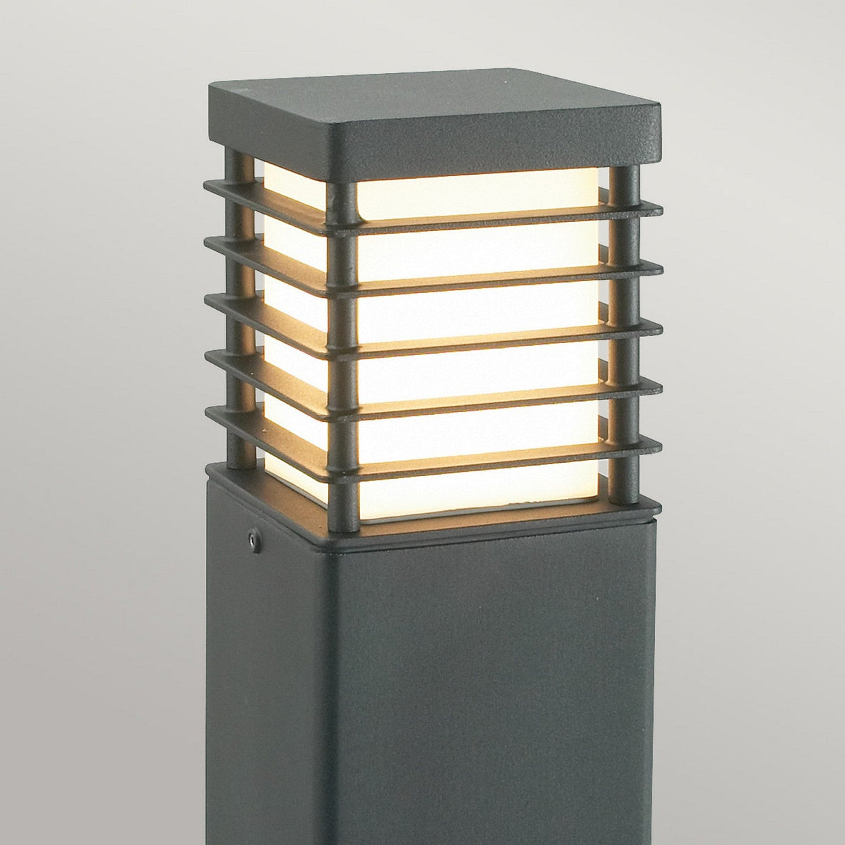 Introducing the Halmstad 1 Light Large Bollard in Black: a weather-resistant outdoor light with a square design featuring horizontal metal slats that encase a glowing white light. This sleek, minimalist piece boasts a dark finish, embodying contemporary style for your modern lighting needs.