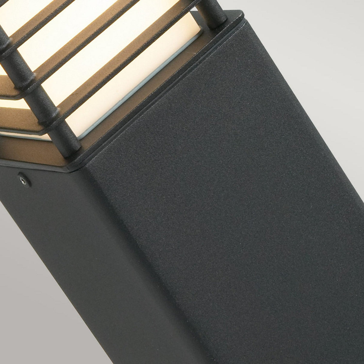 Close-up of the Halmstad 1 Light Medium Bollard, showcasing a modern outdoor design with a rectangular black metal frame and horizontal bars, encasing a white light source. Ideal for enhancing outdoor spaces against a neutral background.