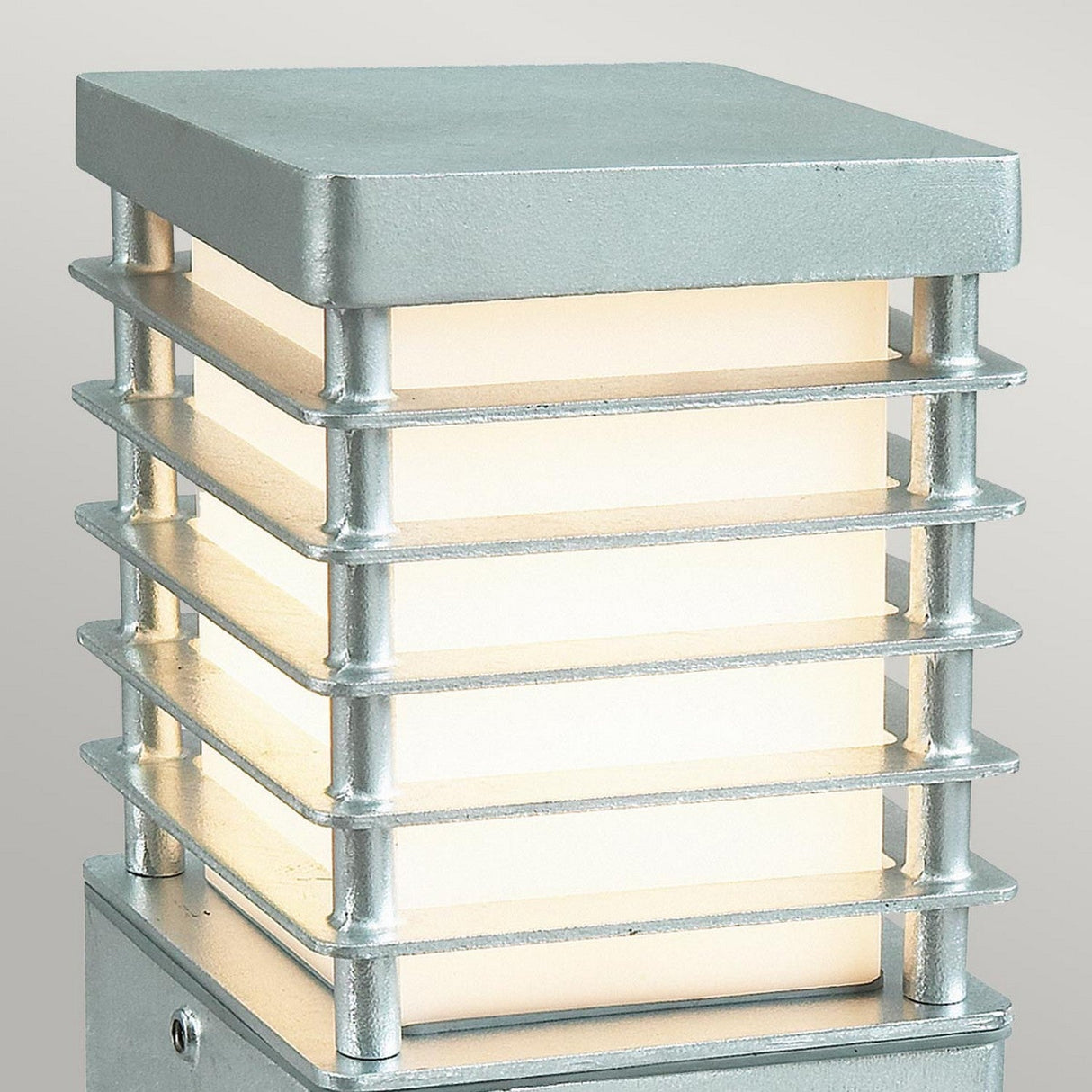 The Halmstad Small Bollard - Silver is a modern outdoor lamp made from galvanized steel, boasting a rectangular frame with horizontal slats. Its frosted glass interior not only provides illumination but also enhances its contemporary style, all while maintaining an IP65 rating for outstanding durability against the elements.