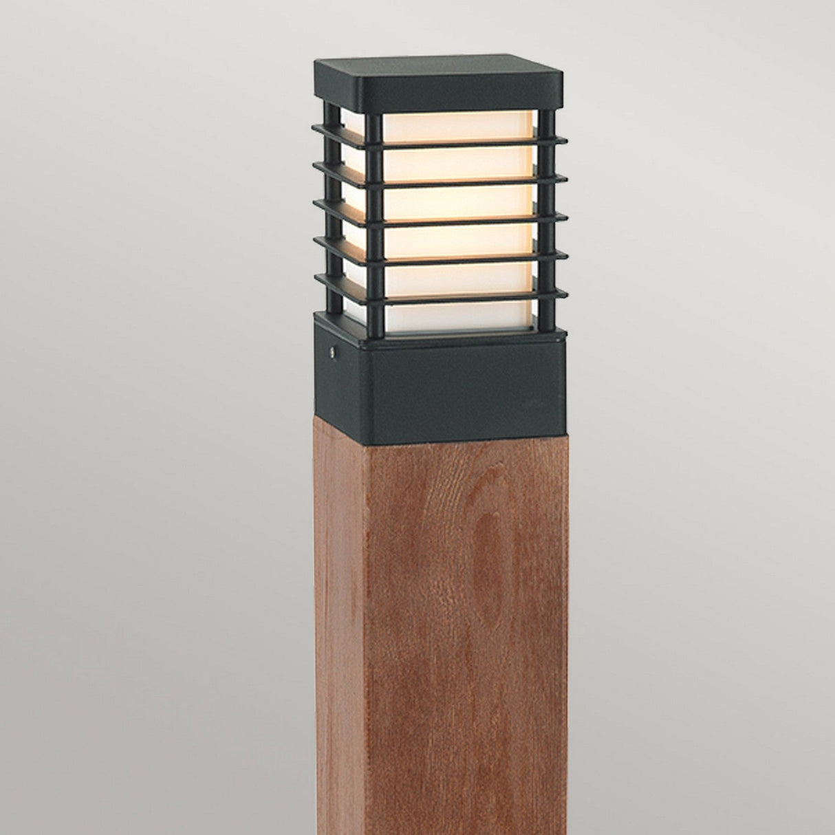 The Halmstad 1 Light Large Wooden Bollard - Black showcases a large wooden structure with a rectangular base, supporting a modern outdoor light. The black metal lantern includes horizontal slats and a frosted glass cover, ensuring durability with its IP65 rating. It offers a minimalist design ideal for chic outdoor lighting.