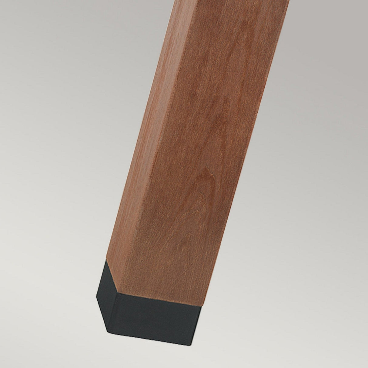 A close-up of the Halmstad 1 Light Large Wooden Bollard - Black reveals its square-shaped structure, reminiscent of a table leg, with a black protective cap at the bottom. The warm brown wood showcases its natural grain, while the cap provides stability and striking contrast.