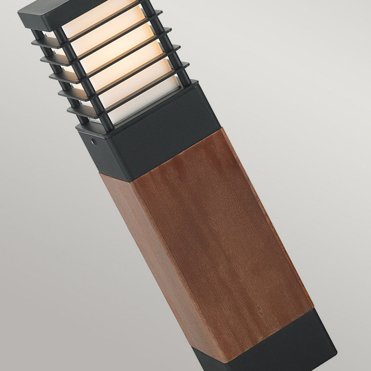Introducing the Halmstad 1 Light Medium Wooden Bollard - Black, a contemporary outdoor lamp featuring a sleek, rectangular wooden design with a black metal frame. Its top section radiates a soft white light, making it an elegant choice for pathway lighting against neutral backdrops.