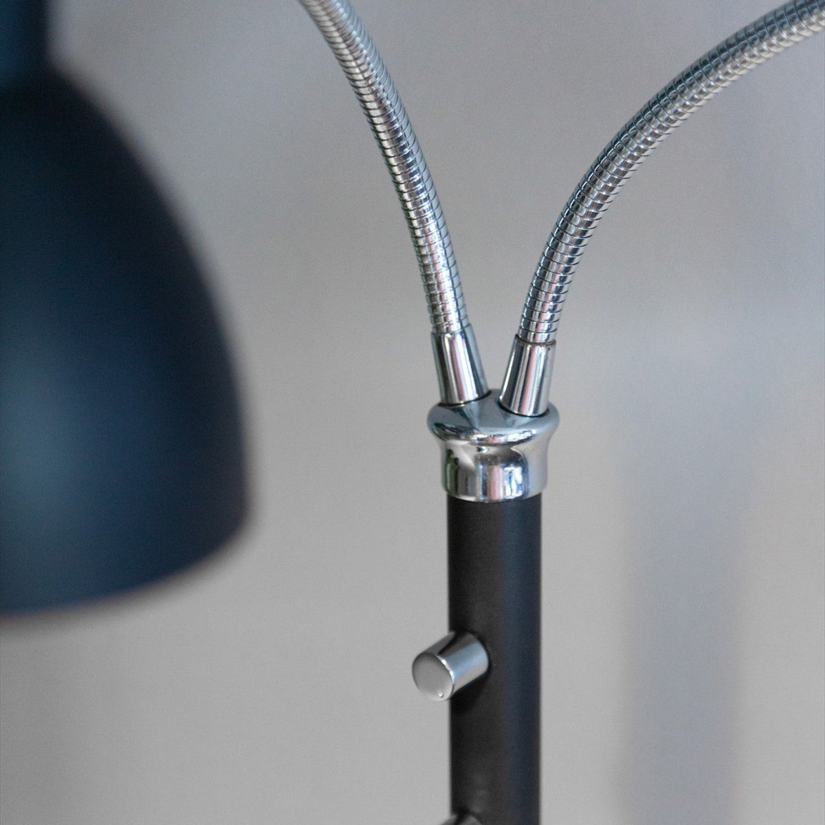 Close-up of the Hudson 2 Light Floor Lamp in black, showing chrome gooseneck arms rising from a chrome sleeve on a matte black column with a control knob.