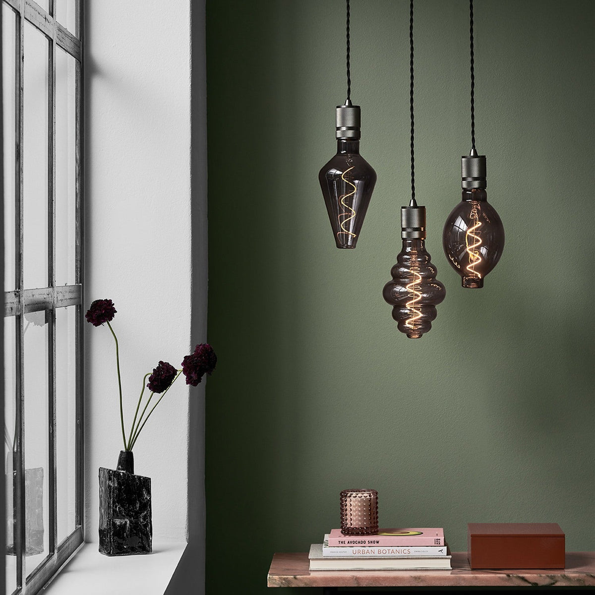 Halo Cable Cord Set E27 pendant fittings in gunmetal with twisted black flex, shown with decorative smoked glass bulbs hanging against a green wall in a styled room.