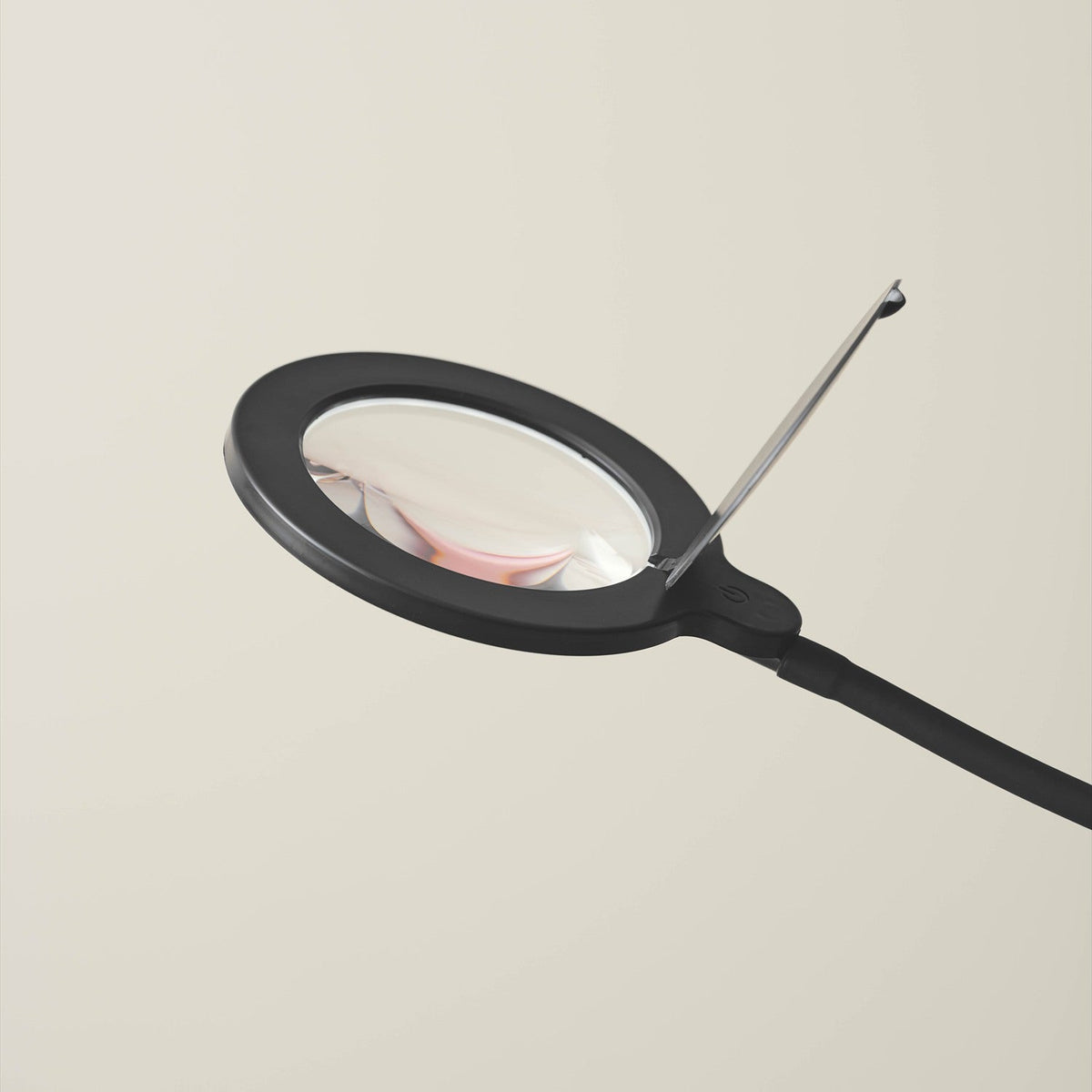 Magni LED X3 Dioptri Floor Lamp in black, close-up of the round magnifying lens head with lit border and hinged cover, mounted on a slim curved stem, shown against a plain light background.