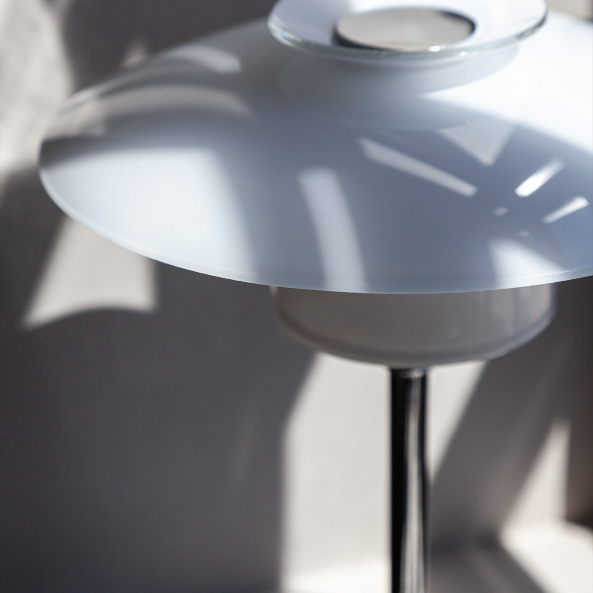 Close-up of the Scandinavia Table Lamp 20cm in opal glass and chrome, showing stacked white glass plates on a polished chrome stem with light shadows on a plain wall.