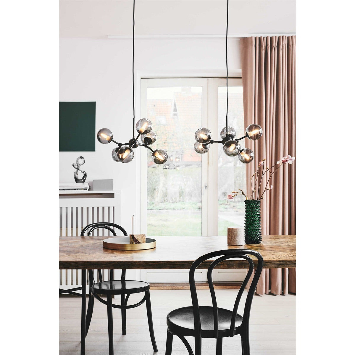 Atom Mini 6 Light Smoke Glass Chandelier in black, branching stubs holding smoked glass spheres at varied angles, shown above a dining table with black bentwood chairs.