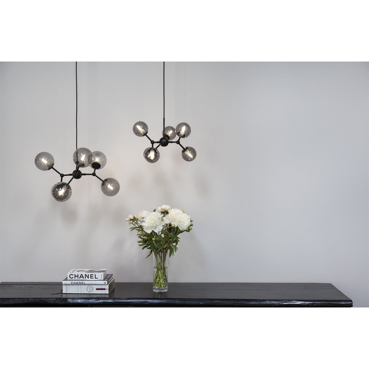 Atom Mini 6 Light Smoke Glass Chandelier in black, shown as two pendants with branching stubs and globes above a black console table in a living room setting.