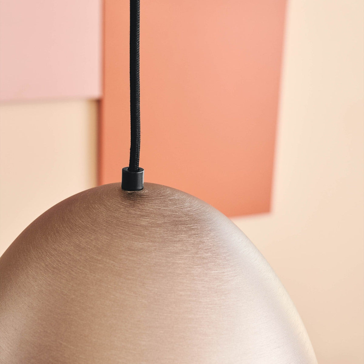 Close-up of The Classic Oxid Brushed Pendant Light 30cm in bronze, showing the domed metal shade's brushed grey-gold finish and black cable mount against a peach-toned background.