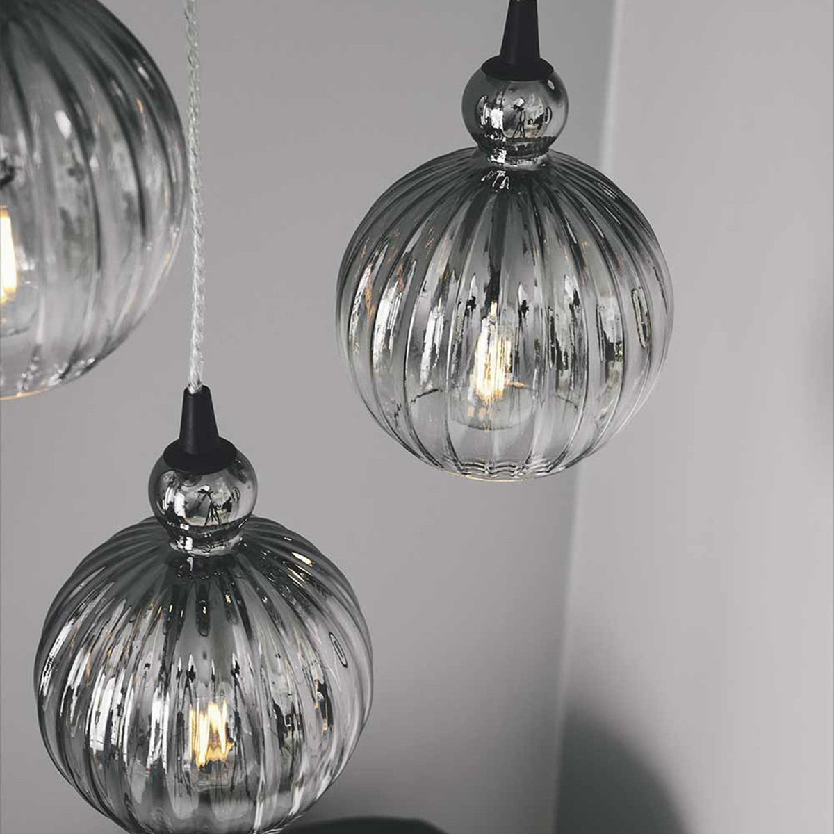 Ball Pendant Light 15cm in smoke shows two ribbed spherical glass shades in soft grey tones with black cone fittings, hung against a light grey wall with visible filament bulbs.