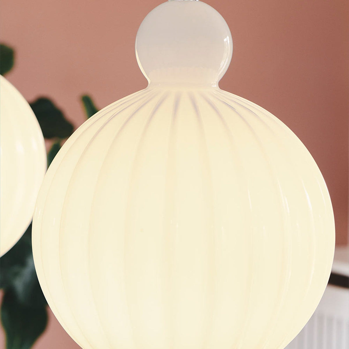 Close-up of the Ball Pendant Light 32cm in opal glass, showing vertical ribbed fluting and a rounded knop with chrome fitting, glowing warm white against a pink wall.