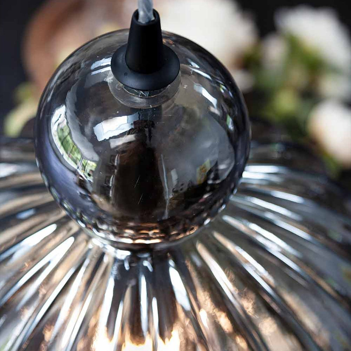 Close-up of the Ball Pendant Light 32cm in smoke, showing ribbed smoked-glass fluting and the black cone fitting with twisted cable against a soft floral background.