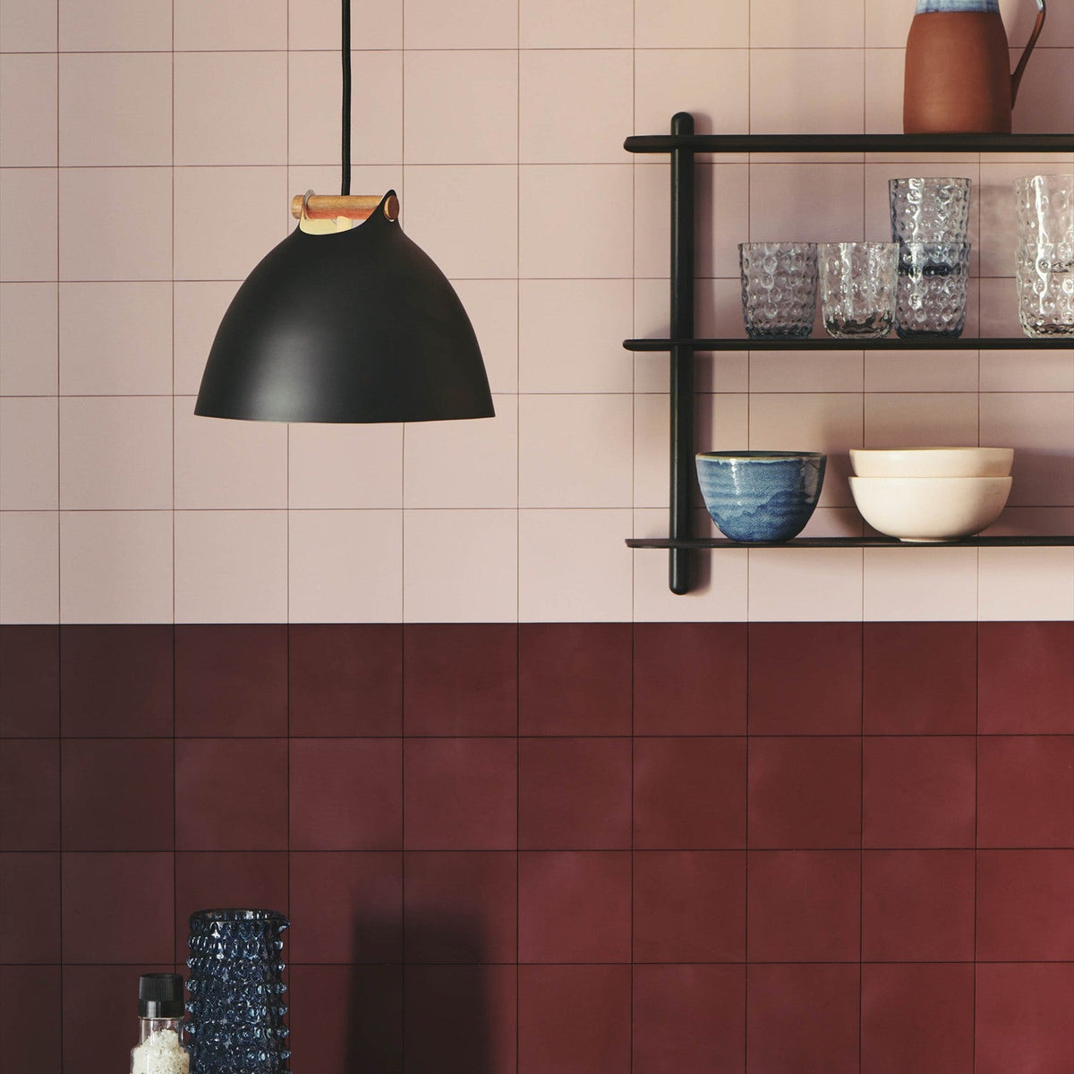 Aarhus Pendant Light 24cm in black with a pale oak strap handle, dome shade with cream interior, hung in a kitchen against pink and red tiled walls.