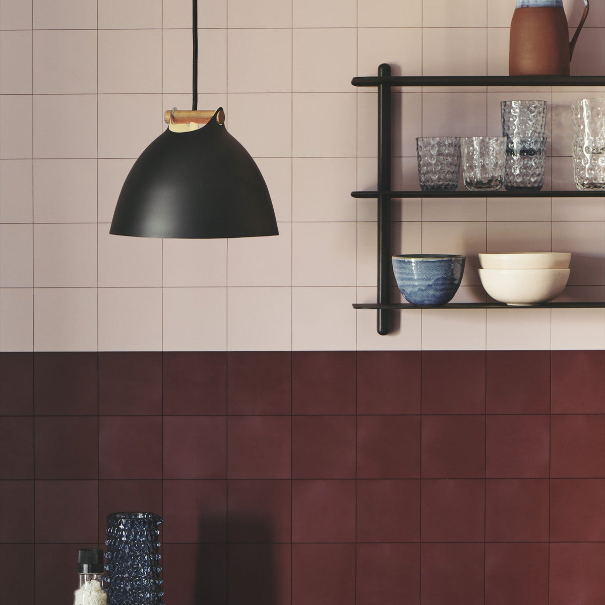 Aarhus Pendant Light 24cm in black with a pale oak strap handle, dome shade shown in a kitchen with pink and burgundy tiles and a black shelving unit.
