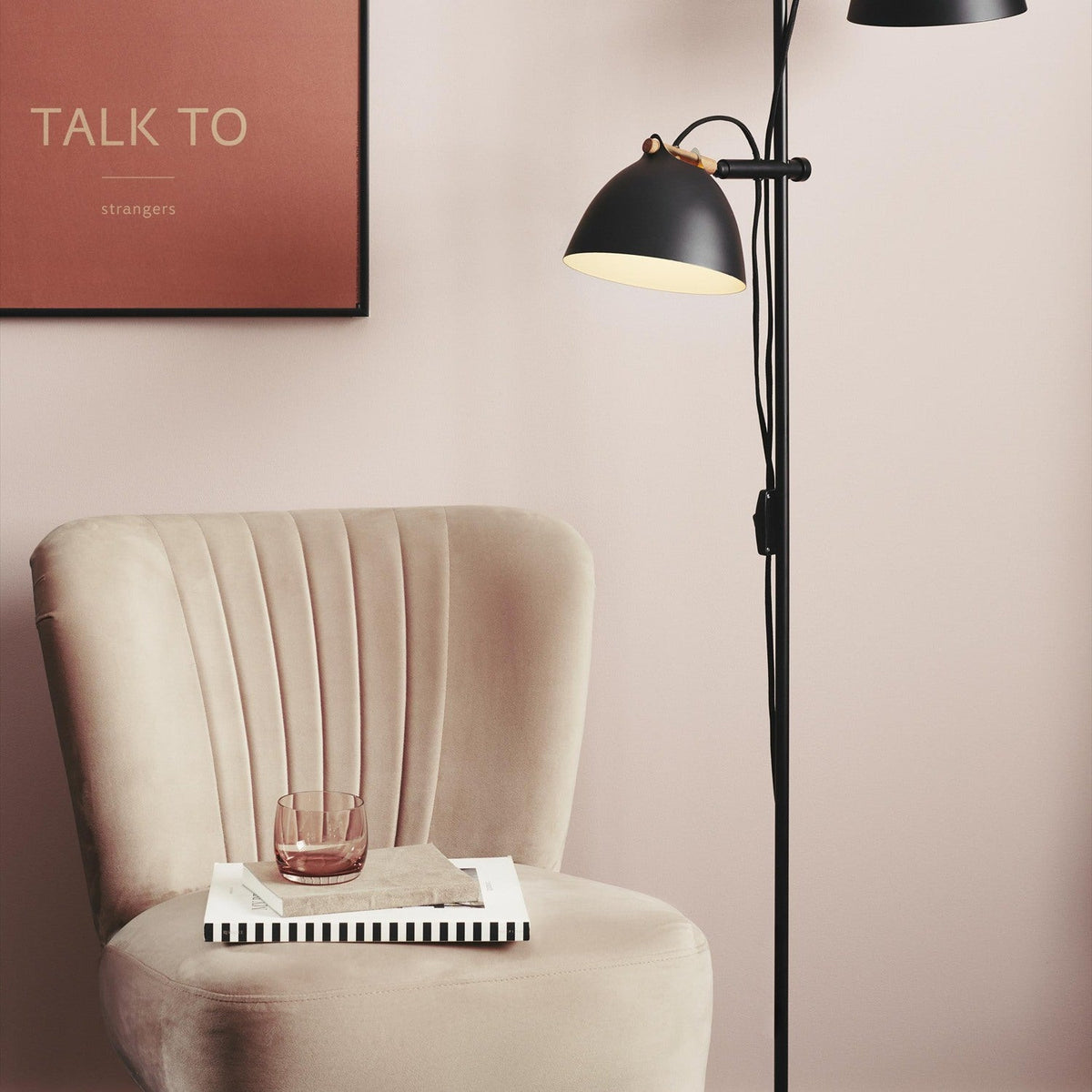 Aarhus 2 Light Floor Lamp in black with wood accent, matt black cone shades with cream interior on a slim stem, shown beside a beige armchair and pink wall.