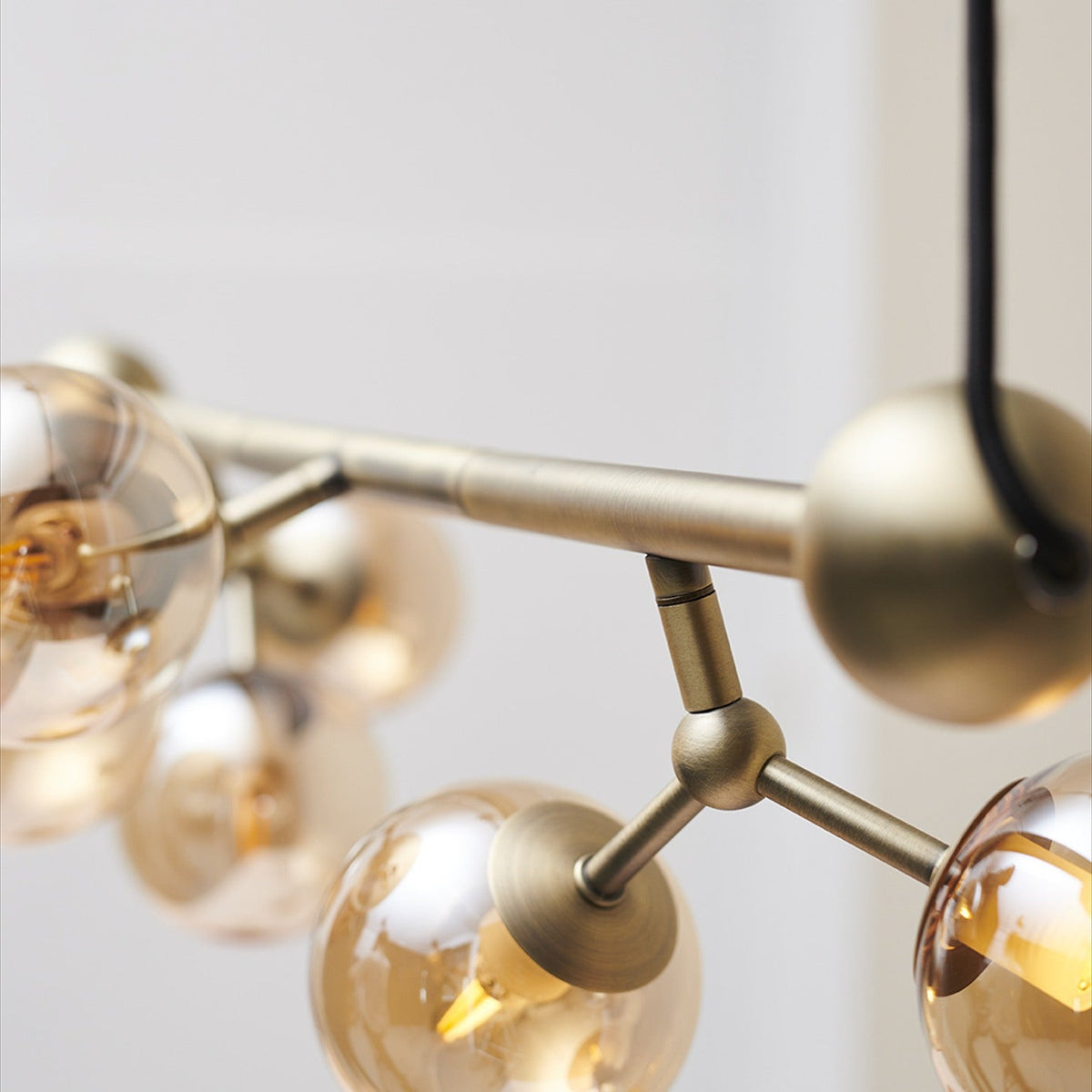 Close-up of the Atom Mini Horizontal 6 Light Chandelier in antique brass, showing the horizontal bar, ball joints, and amber glass spheres against a plain light background.